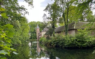 Kasteel verscholen achter geboomte. De toren weerspiegelt in het water van de slotgracht.