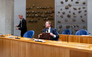 Man in pak zit met een tas op zijn schoot. 