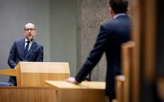 Man in pak staat achter een katheder.