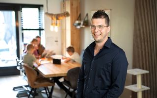 Man in donker overhemd, met op de achtergrond een tafel waar kinderen aan zitten.