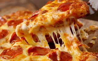 Close-up van een pizza waaruit een punt met gesmolten kaas wordt gehaald.
