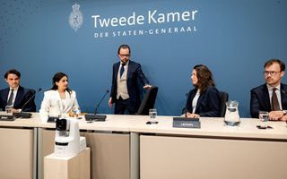De leden van de parlementaire enquêtecommissie over corona zitten achter een tafel. Achter hen een blauwe wand met erop de tekst: Tweede Kamer der Staten-Generaal.