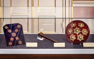 Een ketting op een blauwe ondergrond, een rood schild en een ander voorwerp in een vitrine.
