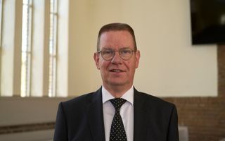 Een man van middelbare leeftijd, met bril, in donker pak met stippeltjesstropdas.