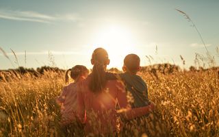 Een moeder en twee kinderen kijken naar de ondergaande zon boven een korenveld.
