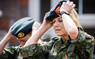 Een blonde vrouw met legergroene outfit zet een donkergroene baret op haar hoofd.