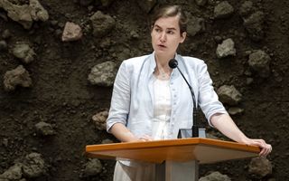 Vrouw met lichtblauwe blouse achter katheder met microfoon in Tweede Kamer.