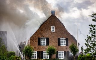 Van een huis met grote ramen komen witte rookwolken. Ervoor is afzetlint gespannen en gaan er waterstralen de lucht in.