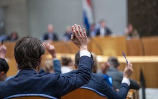 Tweede Kamerlid steekt zijn hand omhoog als teken dat hij vóór stemt
