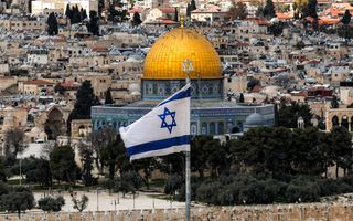 Overzicht van de oude stad van Jeruzalem, met in het midden een gebouw met een goudkleurige koepel. Op de voorgrond een Israëlische vlag.