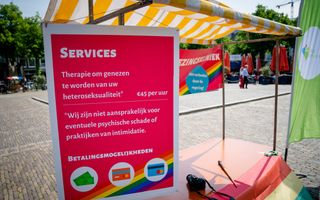 Een kraampje met een groot rood bord waarop witte letters en een regenboog staan.