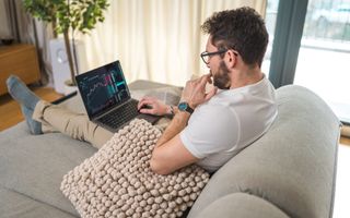 Mannelijke belegger bekijkt aandelengrafieken op een laptop terwijl hij op de bank zit.
