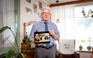 Man met een grijze kuif, een overhemd en een stropdas. Hij houdt een foto vast waarop negen stellen van hetzelfde gezin staan van wie hij het huwelijk sloot.