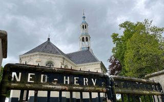 Een oud kerkgebouw met een hoge toren. Op de voorgrond een hek met daarop: Ned – Herv – Kerk.