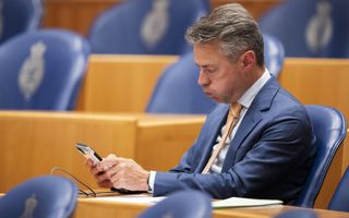 Chris Stoffer kijkt op zijn telefoon terwijl hij op zijn zetel zit in de Tweede Kamer