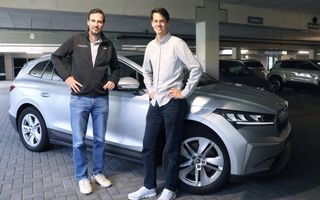 Twee mannen staan in een ontspannen houding voor een grote elektrische auto.