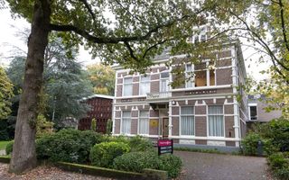Bruin-witte villa tussen bomen.