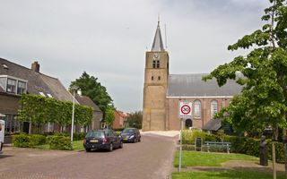 Een straat met geparkeerde auto’s langs de weg en een bakstenen kerk. Aan de zijkant staan groene bomen.
