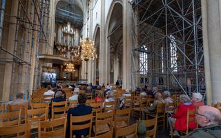 Mensen zitten op stoelen en luisteren in een oude kerk naar een orgel.