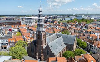 Een kerk met hoge toren staat te midden van woningen met vooral rode pannendaken. De foto is van bovenaf genomen.
