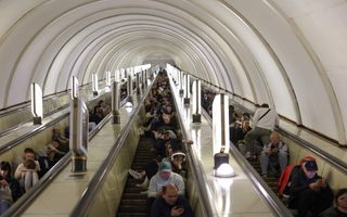 Een grote groep mensen zit op de treden van een trap die toegang geeft tot een ondergronds metrostation.