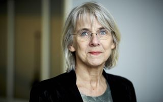 Oudere vrouw met halflang grijs haar en lichte bril. Ze draagt een zwart jasje.