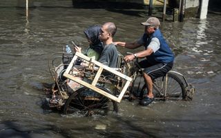 Een bestuurder trapt met een driewielige fietstaxi over een onder water gelopen weg, nadat hevige regenval een rivier buiten haar oevers heeft doen treden.