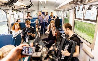 In een trein spelen twee musici respectievelijk accordeon en viool. Mensen luisteren. De musici worden gefilmd.