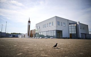 Foto van een vierkant gebouw met daarnaast een minaret met halve maan erop. Op de voorgrond loopt een kauw.