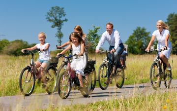 Drie meisjes, gekleed in het wit, en hun ouders fietsen in de zon.