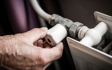 Een hand draait een witte radiatorknop dicht om gas te besparen.