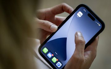 Twee blanke handen houden smartphone vast, duim en wijsvinger goed zichtbaar. Boven in het scherm staat een 112-appicoon. 