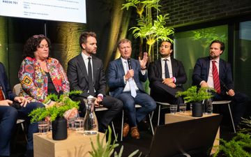 Man met hand omhoog praat in microfoon.