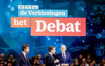 Twee heren voeren een gesprek in een congreszaal terwijl een derde toekijkt