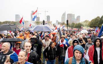 Menigte met vlaggen, erachter torens van kantoorgebouwen.
