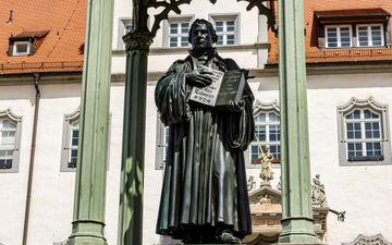 Standbeeld van Luther die een boek vasthoudt. Op de achtergrond een wit gebouw.