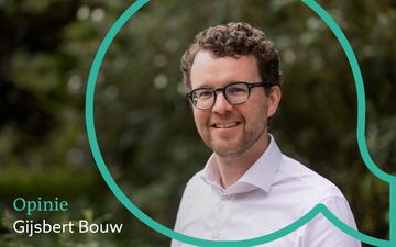 Foto van een man van middelbare leeftijd, donker gekruld haar, bril, baardje, witte blouse, lachend.