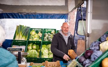 Kale glimlachende man achter een marktkraam. 