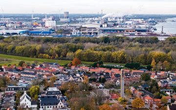 Op de voorgrond een dorp. Blikvanger is een hoge, ranke toren. Op de achtergrond industriegebied.