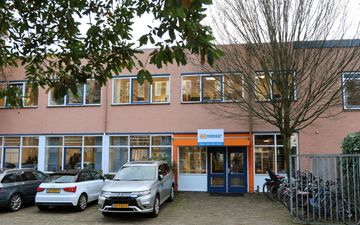 De ingang van een schoolgebouw. Ervoor staan auto’s geparkeerd.
