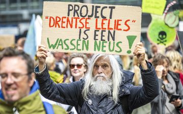 Een man –lang grijs haar en grijze baard– met een kartonnen poster in zijn handen met de tekst „project Drentse lelies is een wassen neus”.