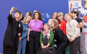 Groep vrouwen lacht voor een selfie. Op de achtergrond een blauwe wand met het logo van de Europese Commissie.