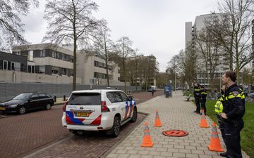 Een politiewagen en enkele agenten op de stoep. Op de achtergrond het schoolgebouw met metalen muur. 