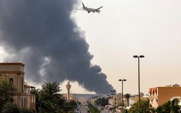 Vliegtuig vliegt langs donkergrijze rookpluim boven stad.