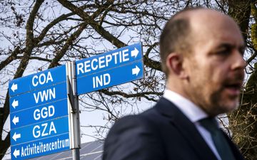 Man in pak staat voor een paal met daaraan blauwe borden met witte letters. 