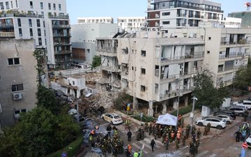 Luchtfoto van mensen in oranje en gele hesjes die naast een beschadigd gebouw hulp verlenen aan slachtoffers.
