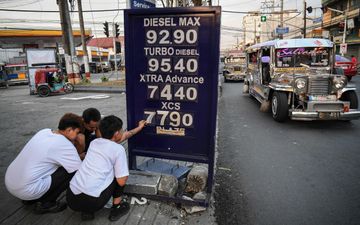 Links drie jonge mannen die een cijfer vervangen van een bord met brandstofprijzen.
