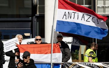 Enkele demonstranten laten een oranje-wit-blauwe vlag zien, evenals een rood-wit-blauwe vlag, met op de witte baan de tekst: ANTI AZC!