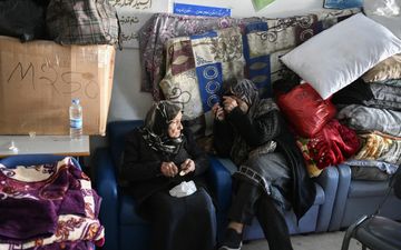 Twee gesluierde vrouwen zitten op bank, naast stapel dekens en kussens.