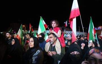 Mensen met rood-wit-groene vlaggen in de hand staan in het donker op een plein.